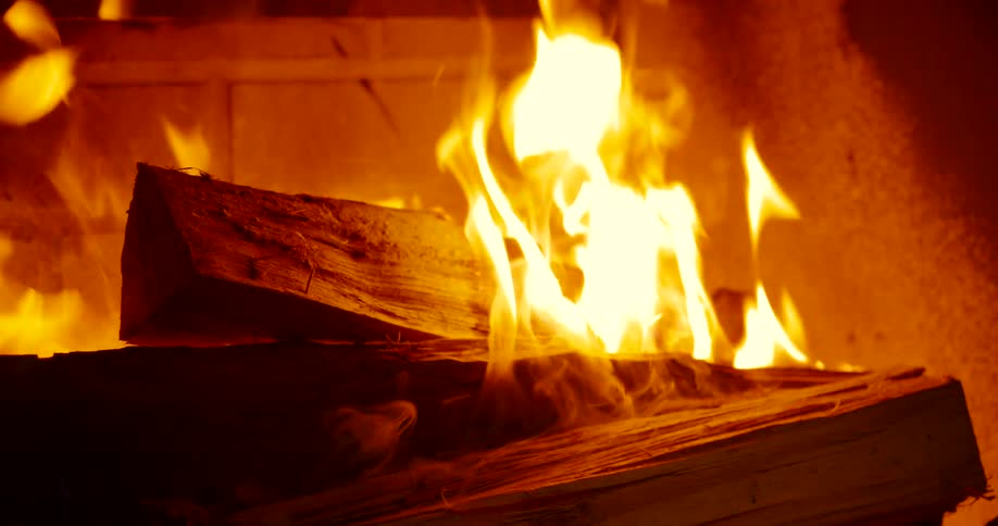 Wood logs are burning in a fireplace with flames and smoke