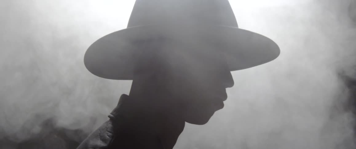 A silhouette of a person wearing a hat with smoke in the background