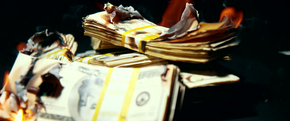 A pile of one hundred dollar bills are engulfed in flames and slowly burn