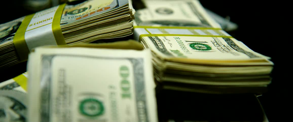 Stacks of hundred dollar bills sit in a pile against a black background