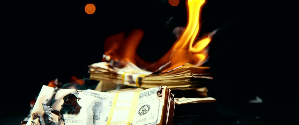 Piles of bills with smoke and flames rising from them