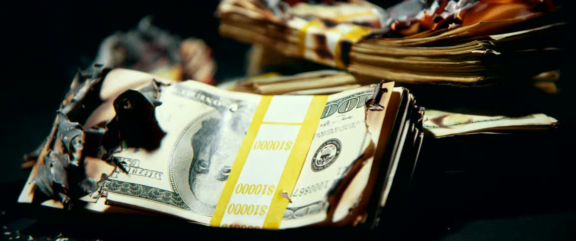 A pile of one hundred dollar bills are on fire and slowly burning