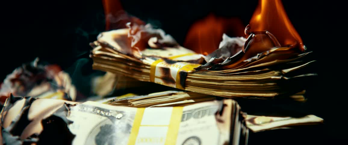 A stack of one hundred dollar bills is on fire and slowly burning up