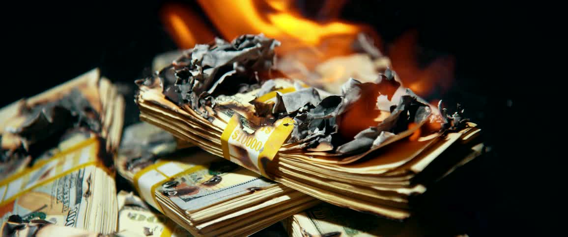 A pile of paper cash money burning to ashes on a dark background