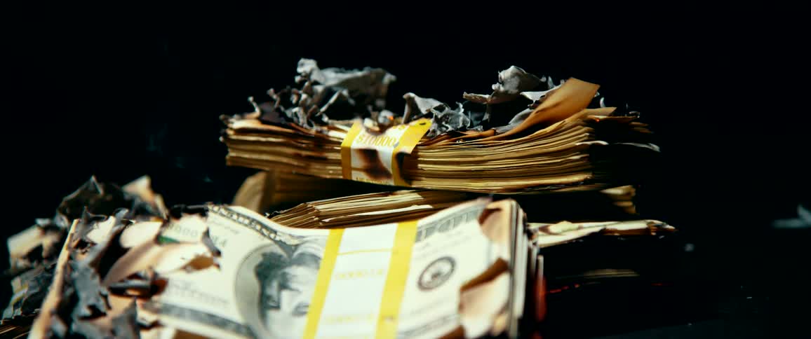 Several stacks of one hundred dollar bills are burned by fire