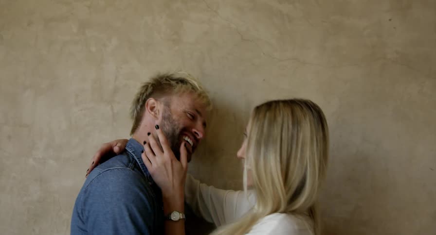 A couple stand next to each other touching and laughing indoors
