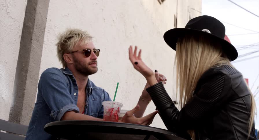 A man and woman sitting at an outdoor table talk while holding hands