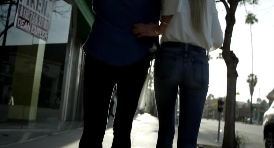 A man and woman walk down a city street with their arms around one another
