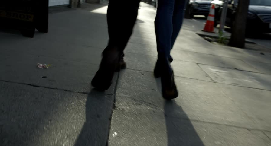 Silhouette of the legs of a couple walking on the sidewalk of a street in the evening