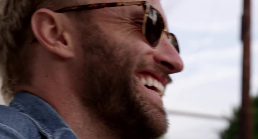 Close up of a bearded young man wearing sunglasses talking and laughingh outdoors
