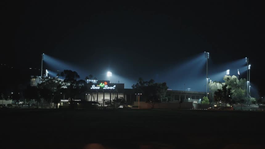 A stadium with spotlights and a flag with trees in the foreground and the sky in the background
