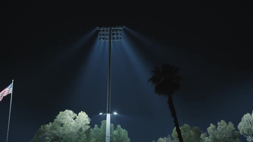 Lights shining brightly and a flag blowing in the wind at a stadium