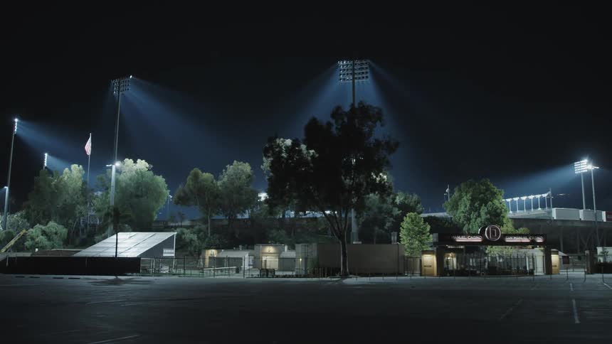 An empty parking lot in front of a stadium with bright lights on