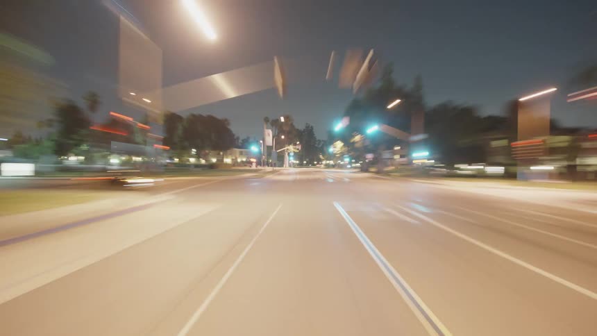 Time lapse of a car driving backwards on a small town road at night
