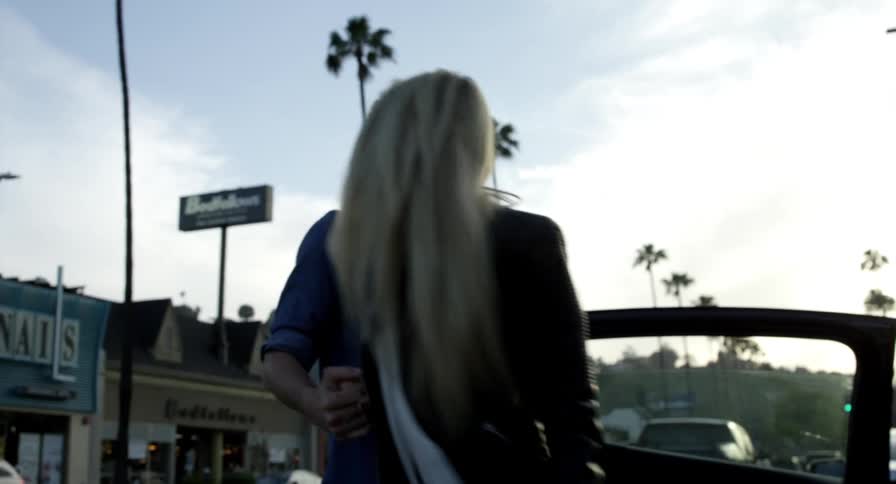 A man and a woman coming out of a vehicle with the street buildings the sky and clouds in the background