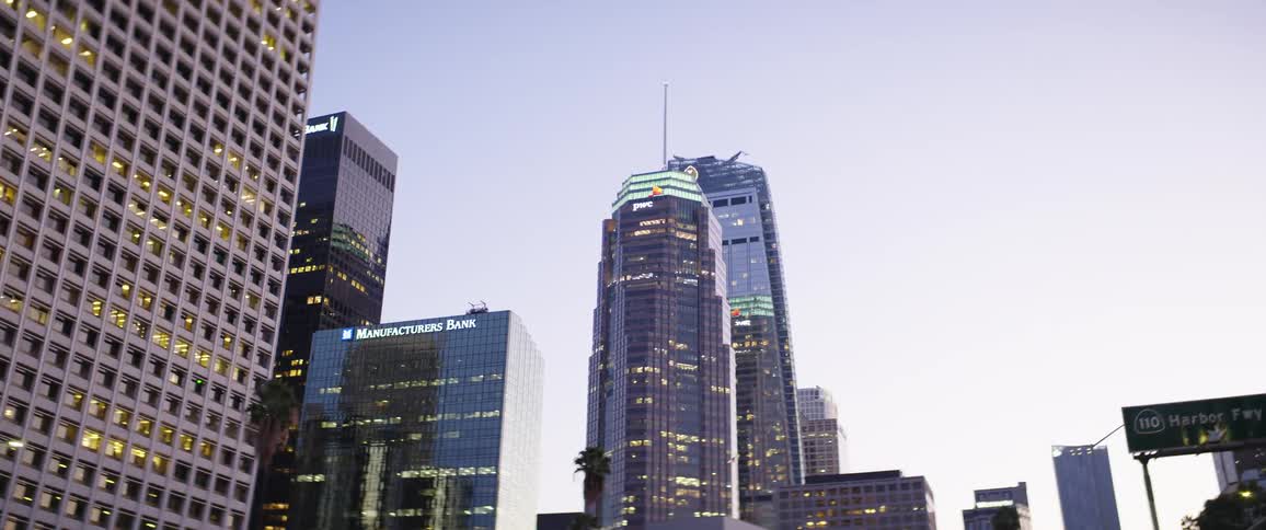 Cars driving on the highway next to the high skyscrapers on the city at sunset