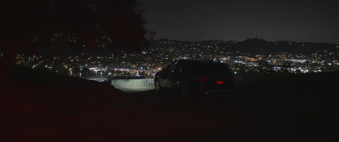 A vehicle parked by a cliff with a city skyline and the sky in the background