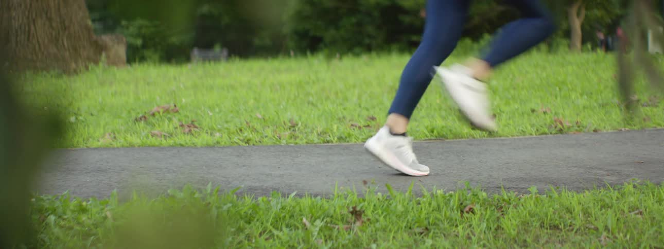 Young fit woman wearing leggings jogging on a path in a park at morning