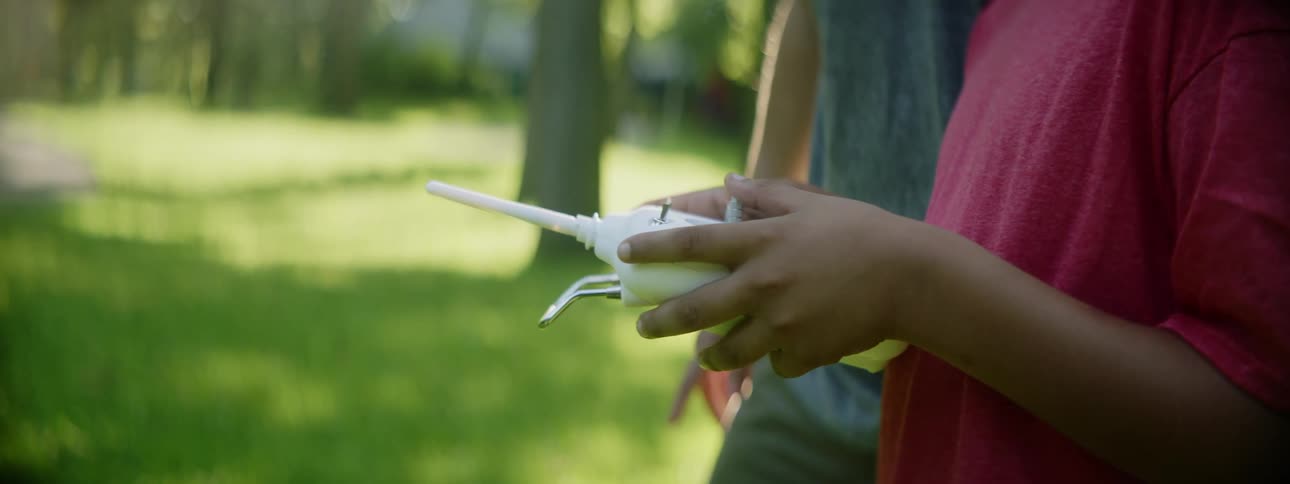 A man watches and stands next to his son as he operates a remote control toy outdoors