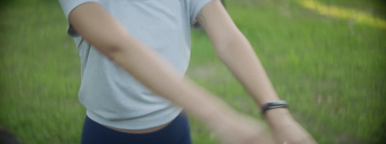 A woman stretched her arms while standing outdoors on a paved path with grass and trees around her