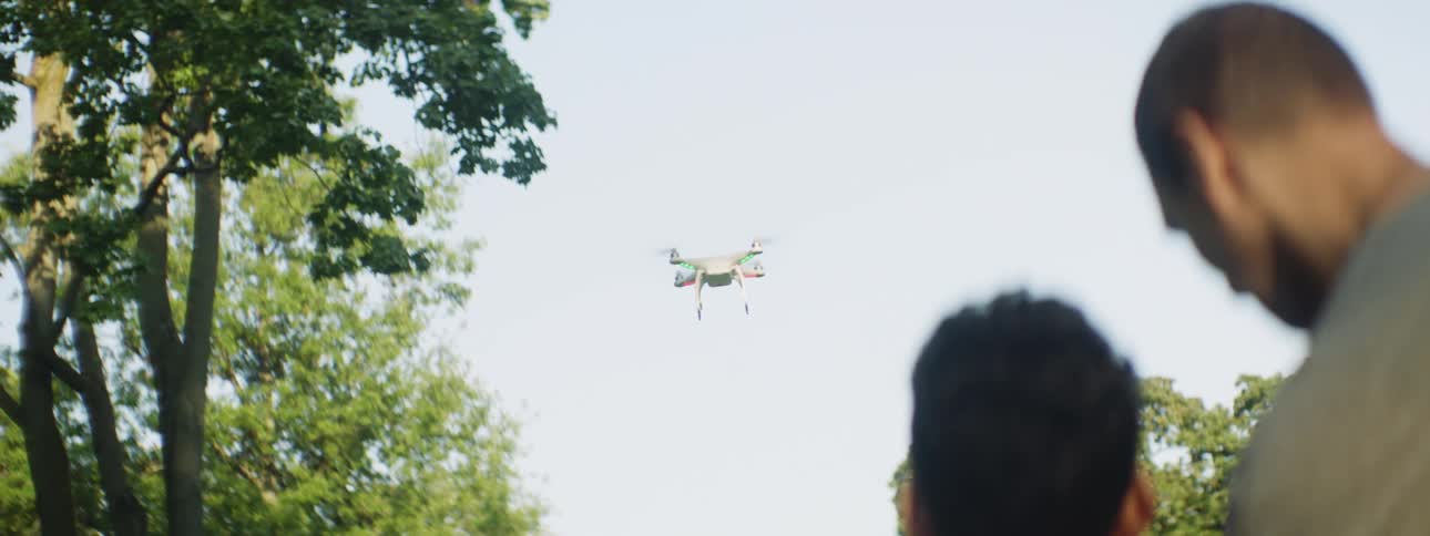Father teaching son how to fly a drone near trees outdoors at day time