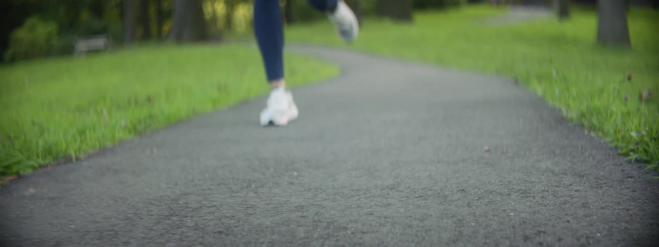 A woman wearing leggings and a t shirt jogs down a paved path outdoors at daytime