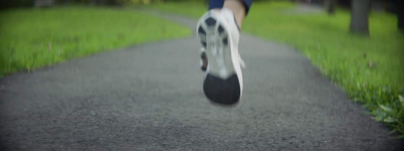 A woman stretches her legs before jogging down a paved path surrounded by trees and grass