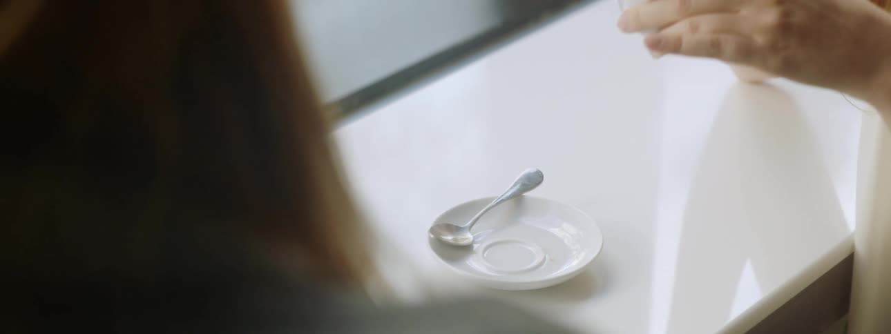 A woman sitting at a table picking up a teacup with tea