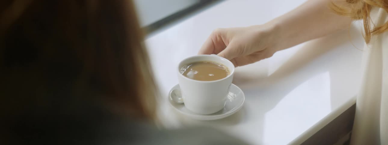 A woman uses a spoon to stir the coffee in a small mug