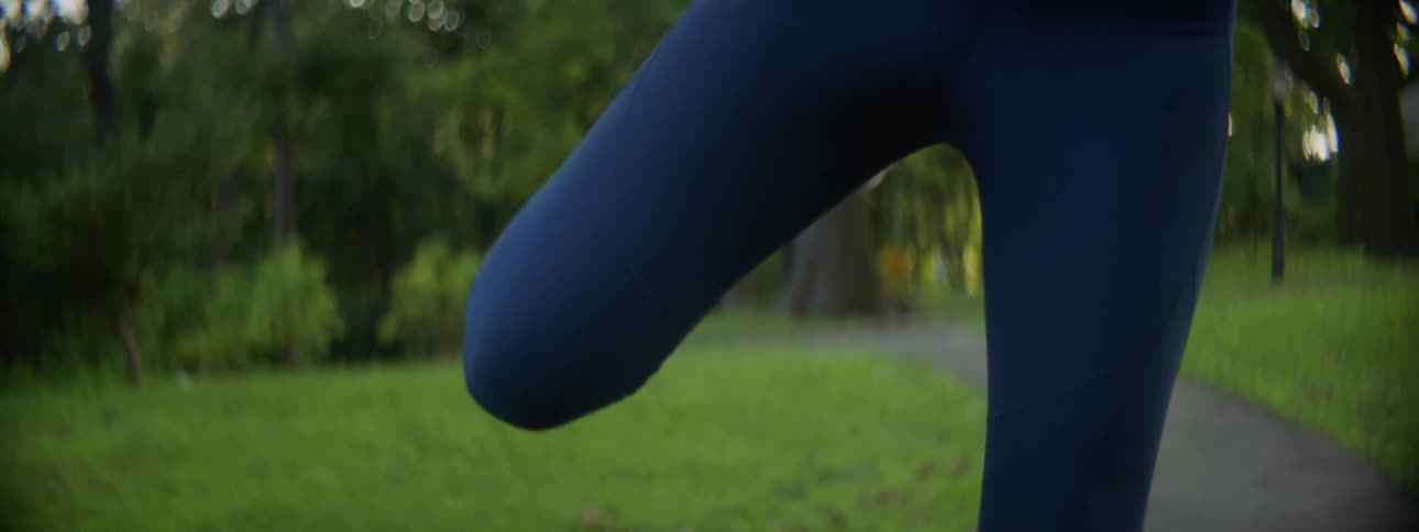 Young fit woman wearing blue leggings stretches before exercising in the park at morning