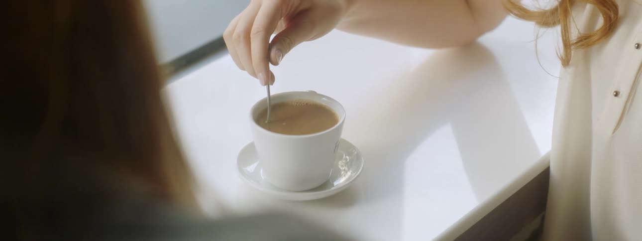 A female hand stirring coffee with a spoon