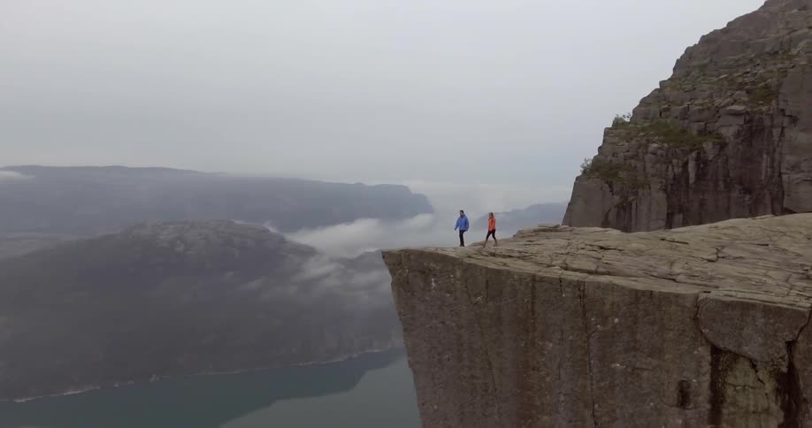 A man and woman walk toward a cliff edge to get a view of a valley far below