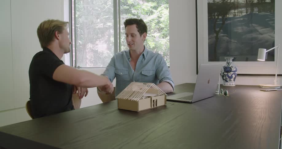 Architect and customer shaking hands on the office in front of a scale model of a house