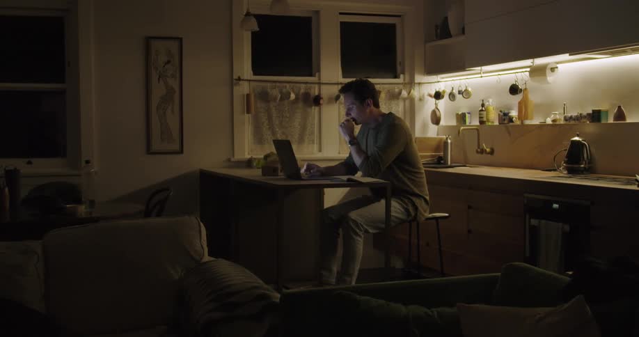 A man at home yawns as he types on his laptop