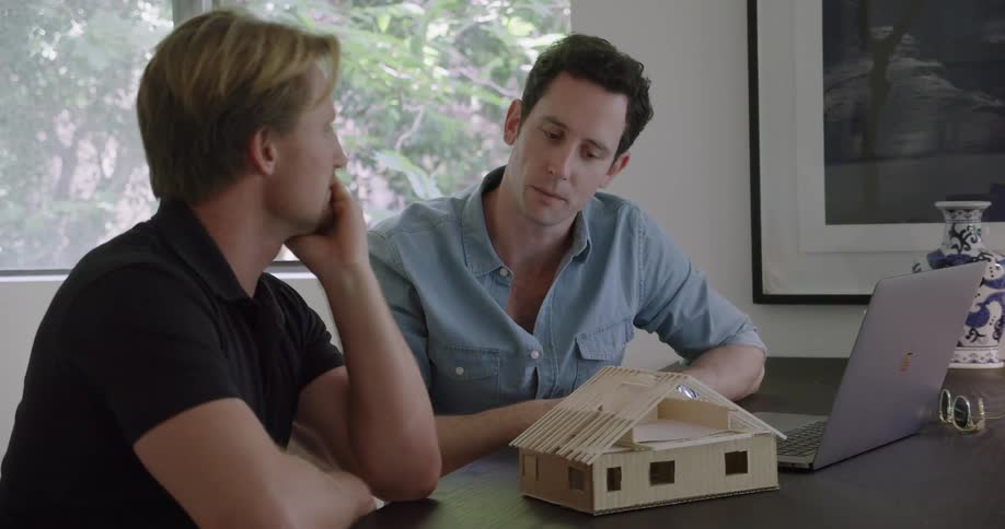 Two men talk and examine a model of a house