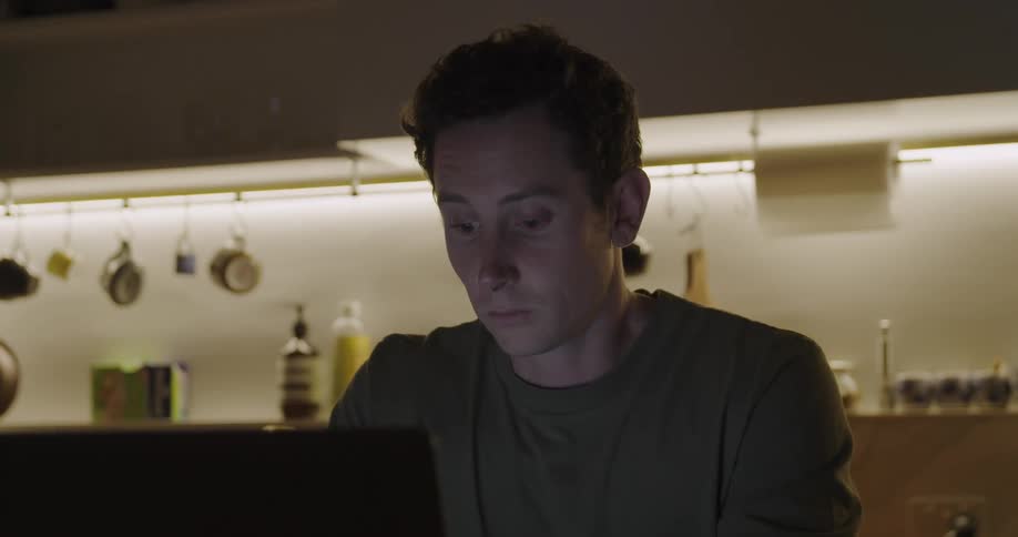 Man working late at night on a laptop sitting at the kitchen table at home