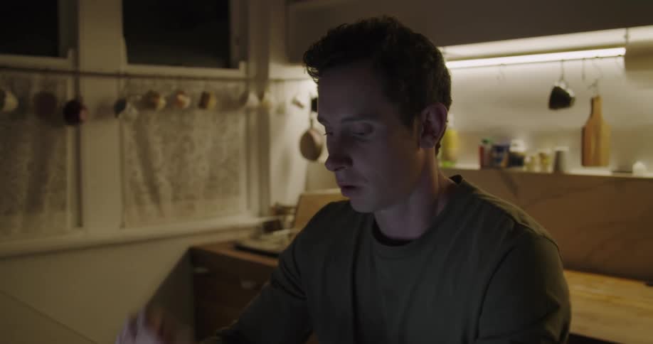 A man sits at a table with a laptop and yawns in exhaustion