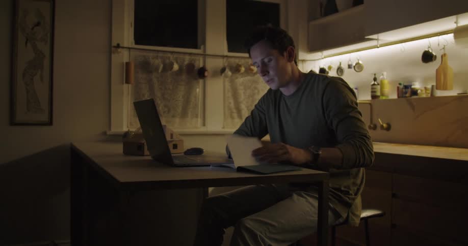 A man looking at both a book and a laptop