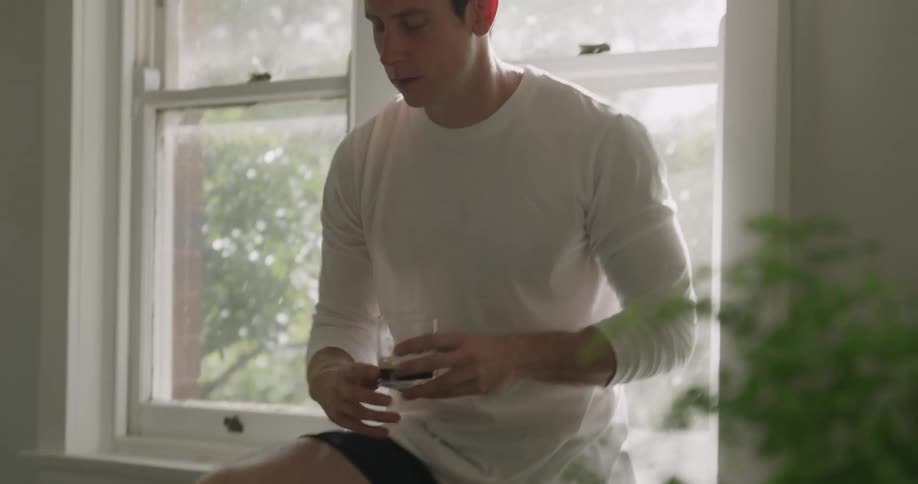 A man types on a laptop using one hand and then takes a drink of water