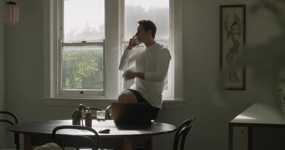 A man at home sets his drink on the table as he talks on the phone