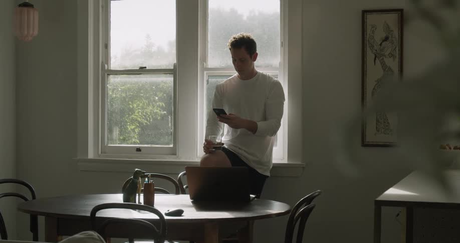 Young man wearing white long sleeve t shirt takes a call on a smartphone at home