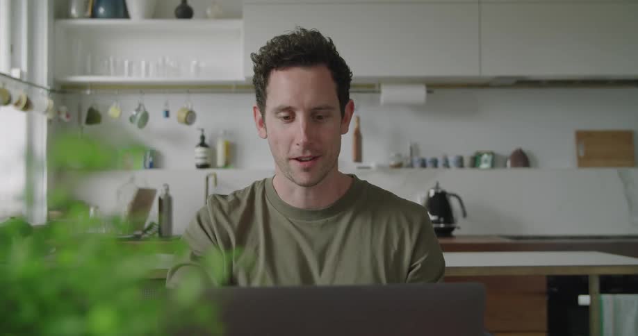 Man sitting at the kitchen table at home says goodbye on a video call in a laptop