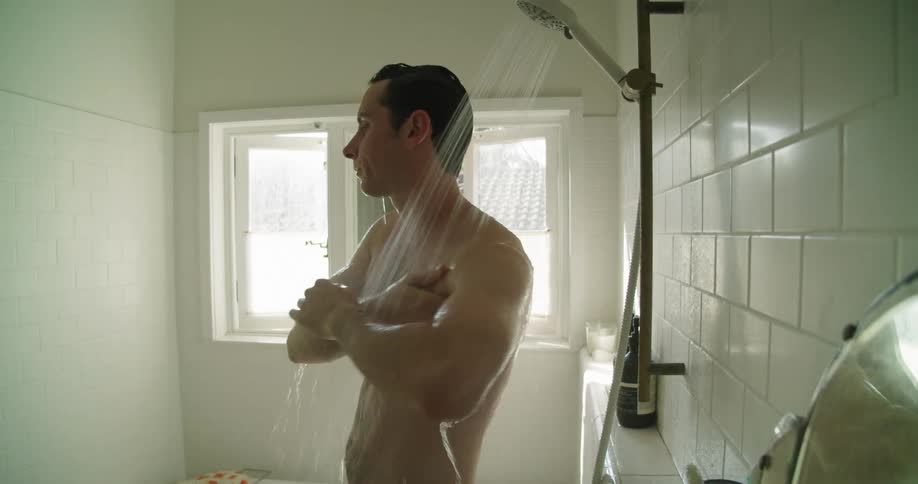 A man runs his hands over his face and hair while showering during the day