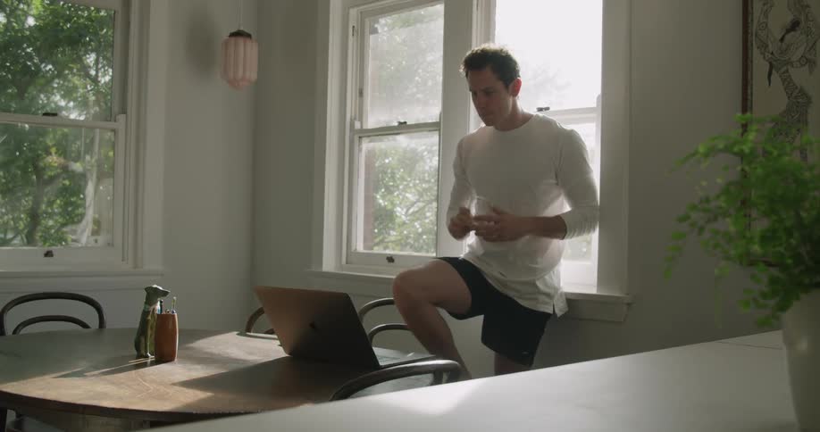 A man is drinking and using his laptop in the dining room