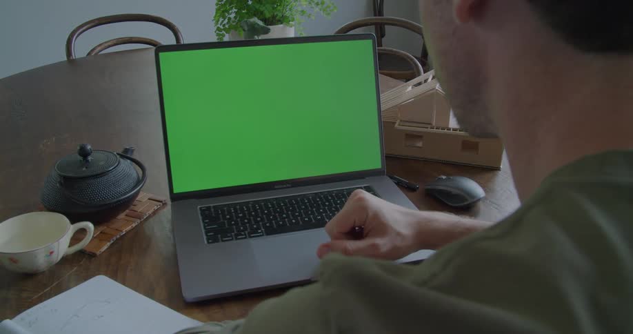 A man works on his laptop while sitting at home at his dining room table