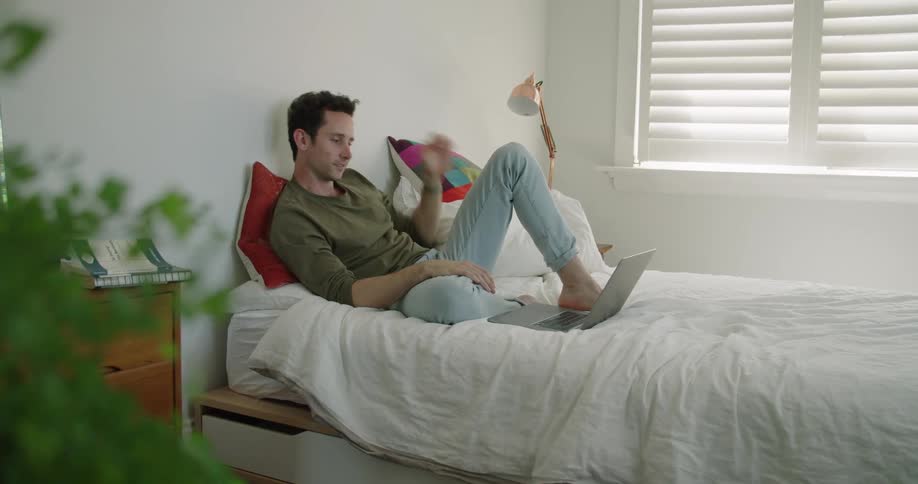 A man relaxing on a bed watching a movie on a laptop