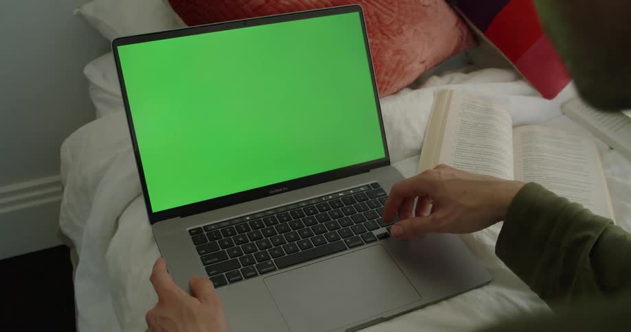 A man at home looks at a green screen on his laptop