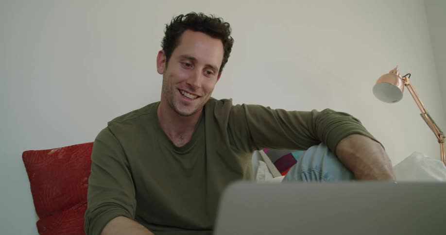 A man sits on his couch at home and chats with someone on his laptop