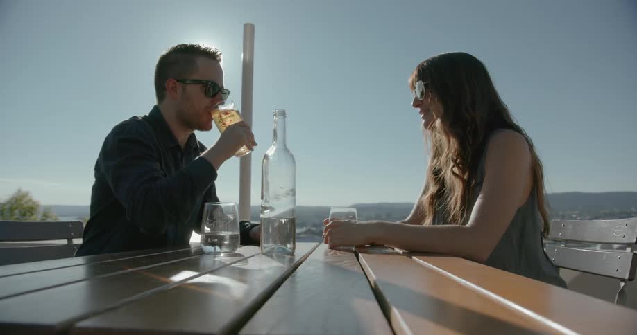 A man and women sit down outside at a table and have drinks