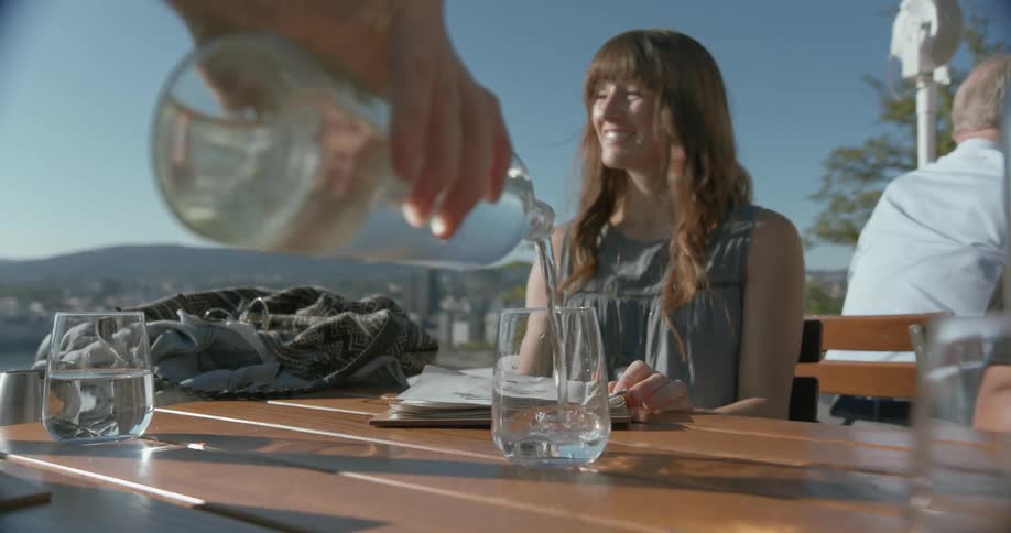 A person pours a drink for a lady in a gray top